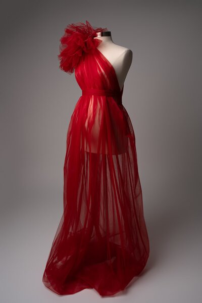 Sheer red gown with tulle overlay and feather detail styled on mannequin for studio maternity photoshoot
