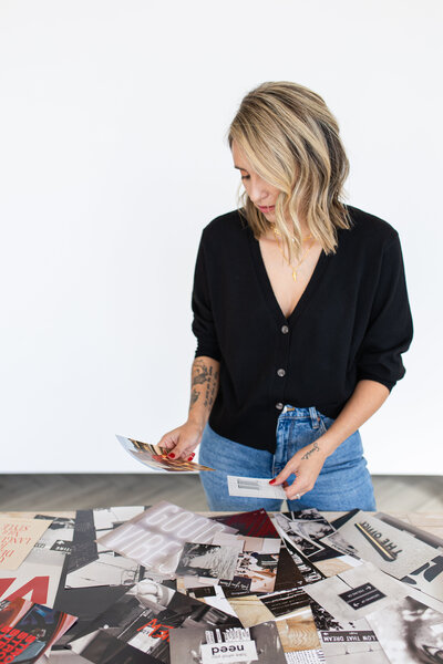 Natalia is in front of a white wall, and in her hands she has paper cutouts with the brand's images on them. She is dressed in a black shirt and jeans.