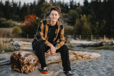Young man sitting on a log at a beach on Whidbey Island.