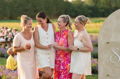 four women in sundresses laughing and smiling and holding drinks during a fundraiser Soiree in the Field. Captured by Ottawa Event Photographer JEMMAN Photography COMMERCIAL 