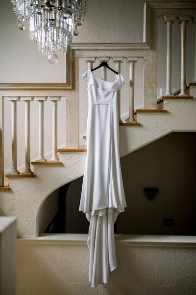 A bride's gown hanging from a staircase with a chandelier 