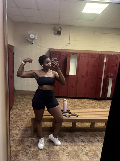 Black career coach flexing right arm in gym locker room