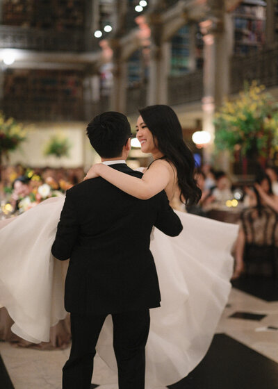 Groom lifting twirling bride during first dance at wedding