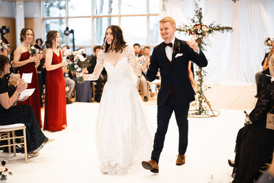 bride and groom smiling and holding hands while walking down aisle