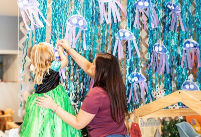 Ms. Brandi helping a young student hang her artowrk in the classroom at the Nest, a preschool in the heart of Surf City, NC