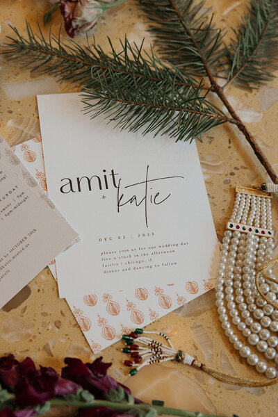 Flatlay includes a rustic wedding invitation, bridal pearls, pine, lace and dried flowers.