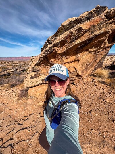 Woman wearing wide-brimmed black hat and orange sports bra smiles at the camera in Castle Valley, Utah.