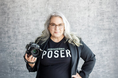 Female photographer holding camera wearing a shirt that reads "Professional Poser"