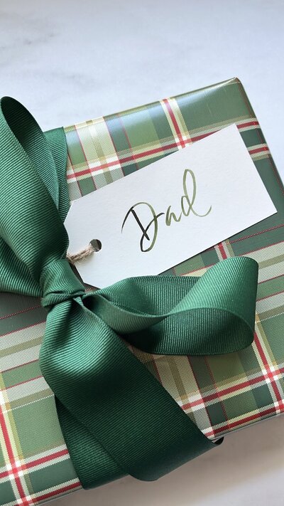 Green plaid gift with green grosgrain ribbon and white gift tag with green watercolor calligraphy.