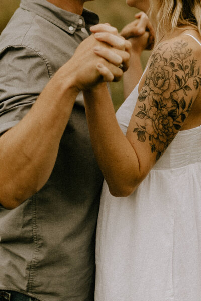 Close-up image of a couple with tatoos holding hands