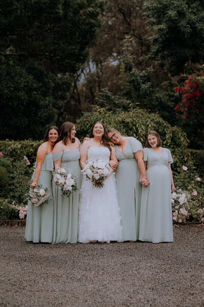 Bride with her bridesmaids in sage green dresses standing together and cuddling