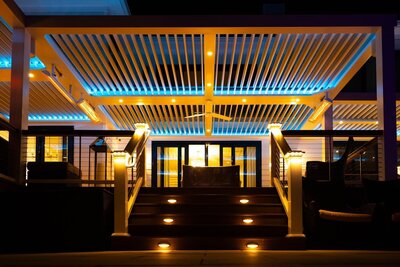 Low-angle view of a white StruXure pergola at night, illuminated by integrated lights and blue LEDs from the TraX system. 