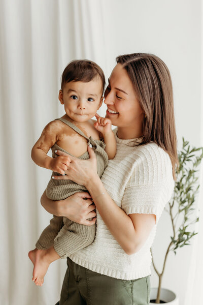 A mom holds and smiles at her one year old baby during his first birthday photoshoot inside a Vancouver Washington studio