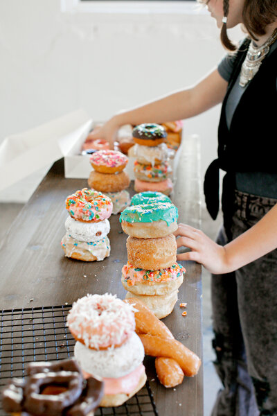 Hands Stacking Donuts on Countertop - Daylight Donuts
