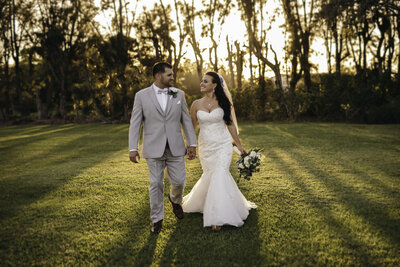 bride and groom holding hands while walking through field