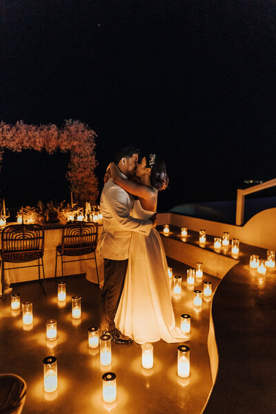 Bride and groom dancing on balcony in Santorini surrounded by candles