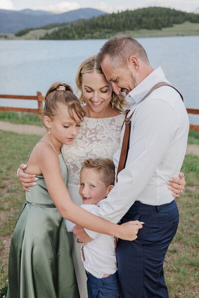Bride, groom, and their kids enjoy family hug after wedding ceremony.