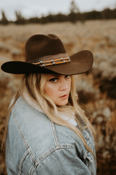 woman holding hat and smiling at the camera