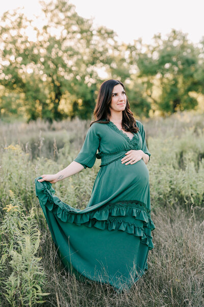 Expecting mom is wearing a green baltic born dress while standing in a beautiful green field