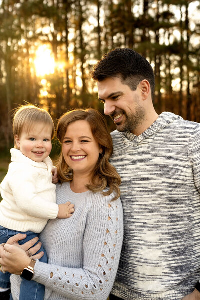 Mother holding young son and smiling at camera while father looks at them by Atlanta family photographer