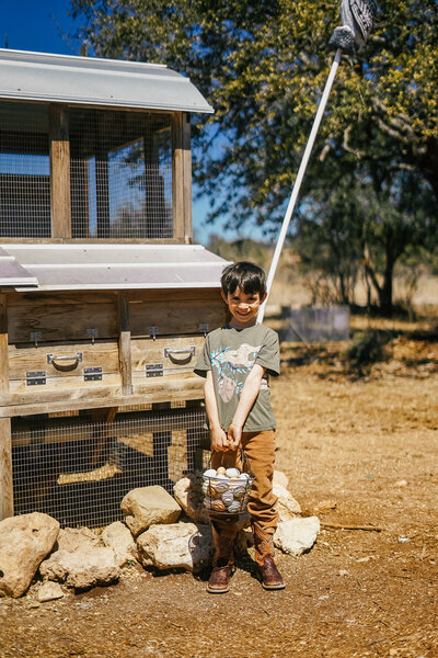 Young boy holding a basket of eggs outside a chicken coop
