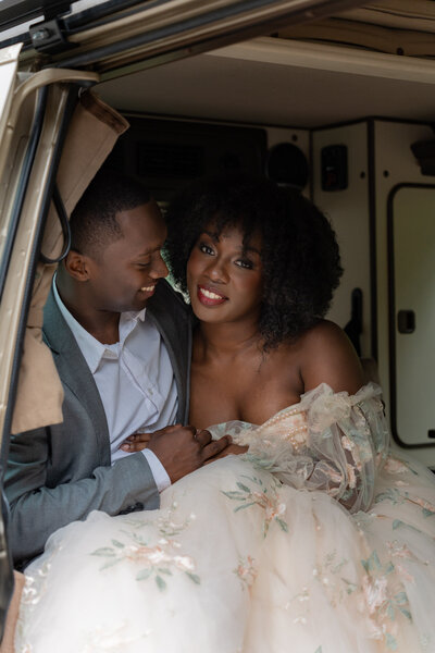 A newlywed couple sitting in the back of a camper van