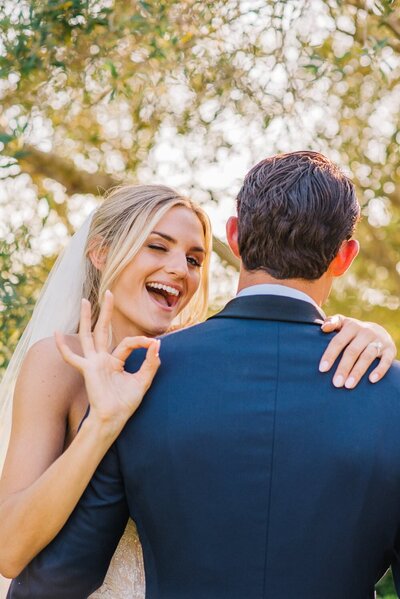 Bride smiles and signals over her grooms shoulder on their wedding day