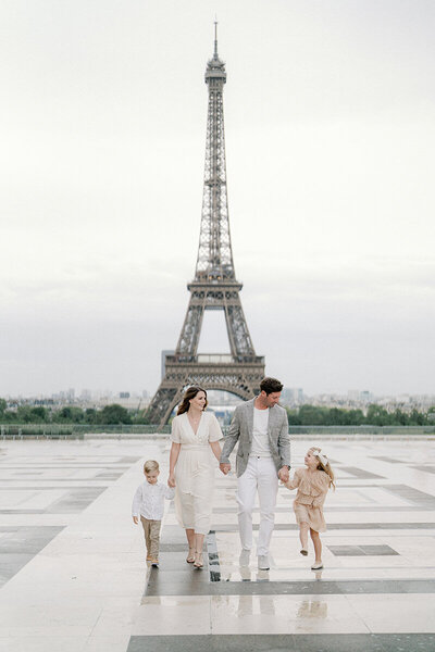a family holding hands and walking towards the camera with the eiffel tower in the background