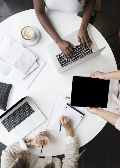 group of people working at a white round table with their laptops out, along with notebooks and coffee