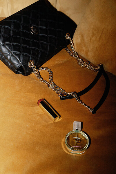 A black purse, lipstick, and perfume bottle sitting on a yellow velvet couch