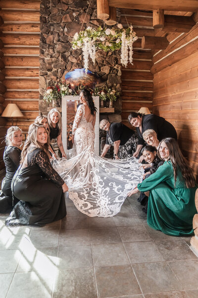 Charming photograph capturing bridesmaids holding out the bride's dress, showcasing its intricate details and adding a touch of elegance to the wedding day.