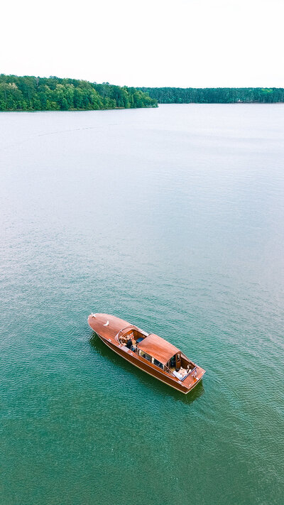 Lake oconee boat wooden boat sits on teal waters with couple cuddling during engagement sesion
