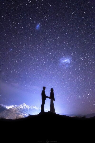 Astrophotography portrait of a couple in among the mountains in front of a starry night