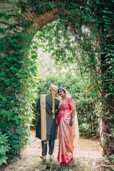 Couple in traditional Indian wedding attire posing under greenery arch