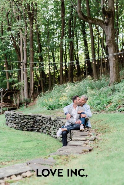 A man sits behind his partner and kisses his cheek