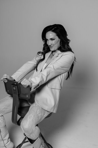 A black and white photo of Juliet Trnka sitting on a chair in a playful, fun manner