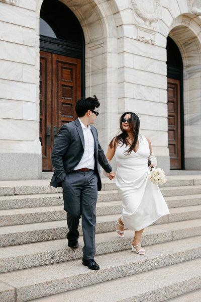 Bride and groom holding hands running down courthouse steps
