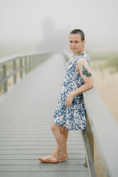 Jeanne Sager stands on a beach walkway. On her arm is a photographer's tattoo of a gnome and a Nikon camera