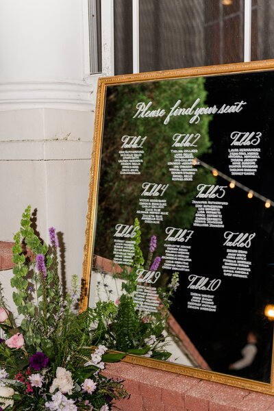 Mirror with calligraphy wedding seating chart with gold frame and purple flowers