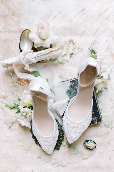 wedding flatlay with white bridal shoes and flower and pearls around it