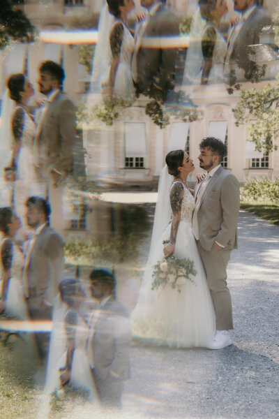 Das Foto zeigt ein Hochzeitspaar in einer Umarmung vor Schloss Nymphenburg mit einem Prisma-Effekt.