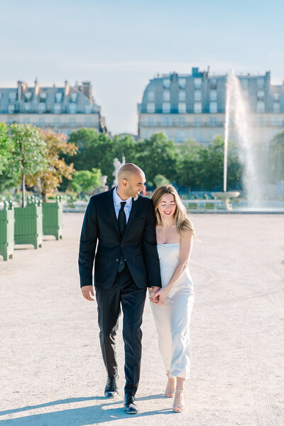 Man and woman holding hands while walking by a fountain during a romantic Paris couples photoshoot near the Eiffel Tower and Tuileries Garden.