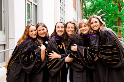 Six senior girls standing outside of Vanderbilt Law School smiling at camera wearing their master's robes