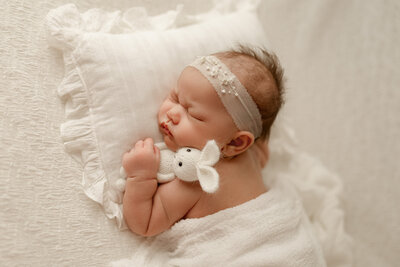 Newborn baby girl peacefully swaddled in soft pink wrap, resting in a heart-shaped bowl during a styled studio session by Duehr Photography in Maple Grove,MN