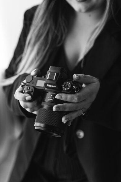 Black and white photo of a photographer holding a camera at mentoring for newborn photographers