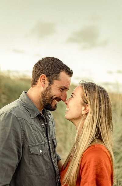 A man and woman embracing outdoors for an engagement photoshoot, showing love and happiness. The man has a beard and they are smiling at each other.