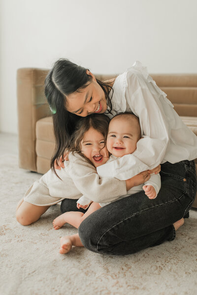 Mother hugging two young children, smiling joyfully
