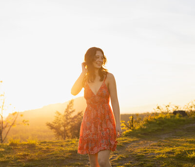 lovely girl in a red dress with brown hair at sunset - golden hour glow and she is laughing looking away from the camera in greenwater washington 
