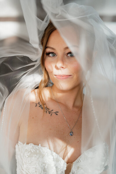Bride wearing her wedding dress with her vail in the air while gently smiling