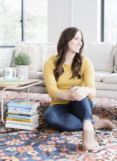 photo of the brand photographer, Laurelyn of My Brand Photographer, sitting on a vintage rug next to a stack of books, wearing a yellow long-sleeved tee and jeans